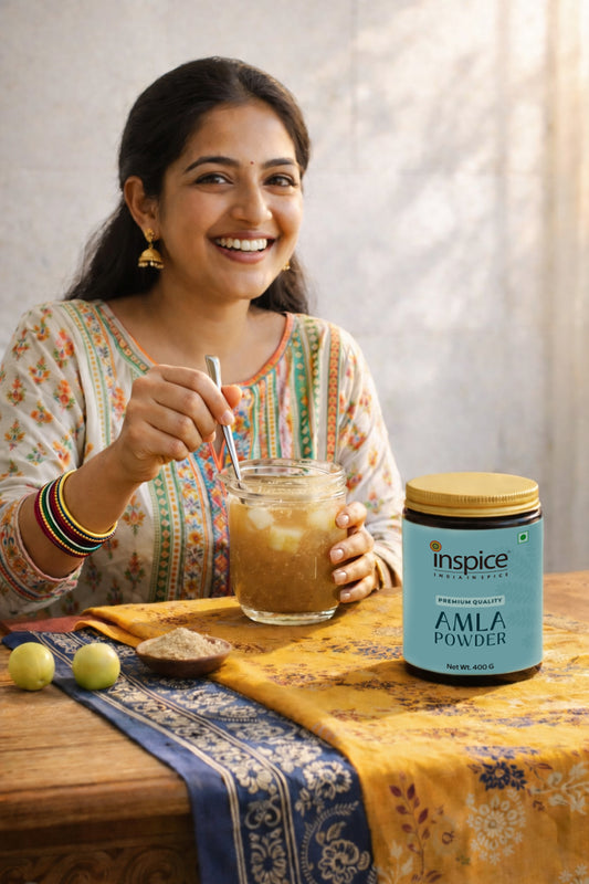 Woman holding a glass of amla powder drink with a container of Inspice Amla Powder on a table.